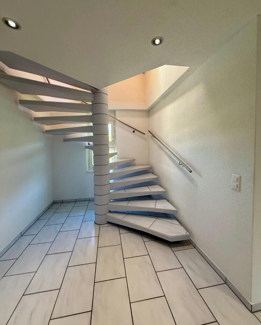 Un escalier moderne au design original, un mur de couleur claire et un sol carrelé.