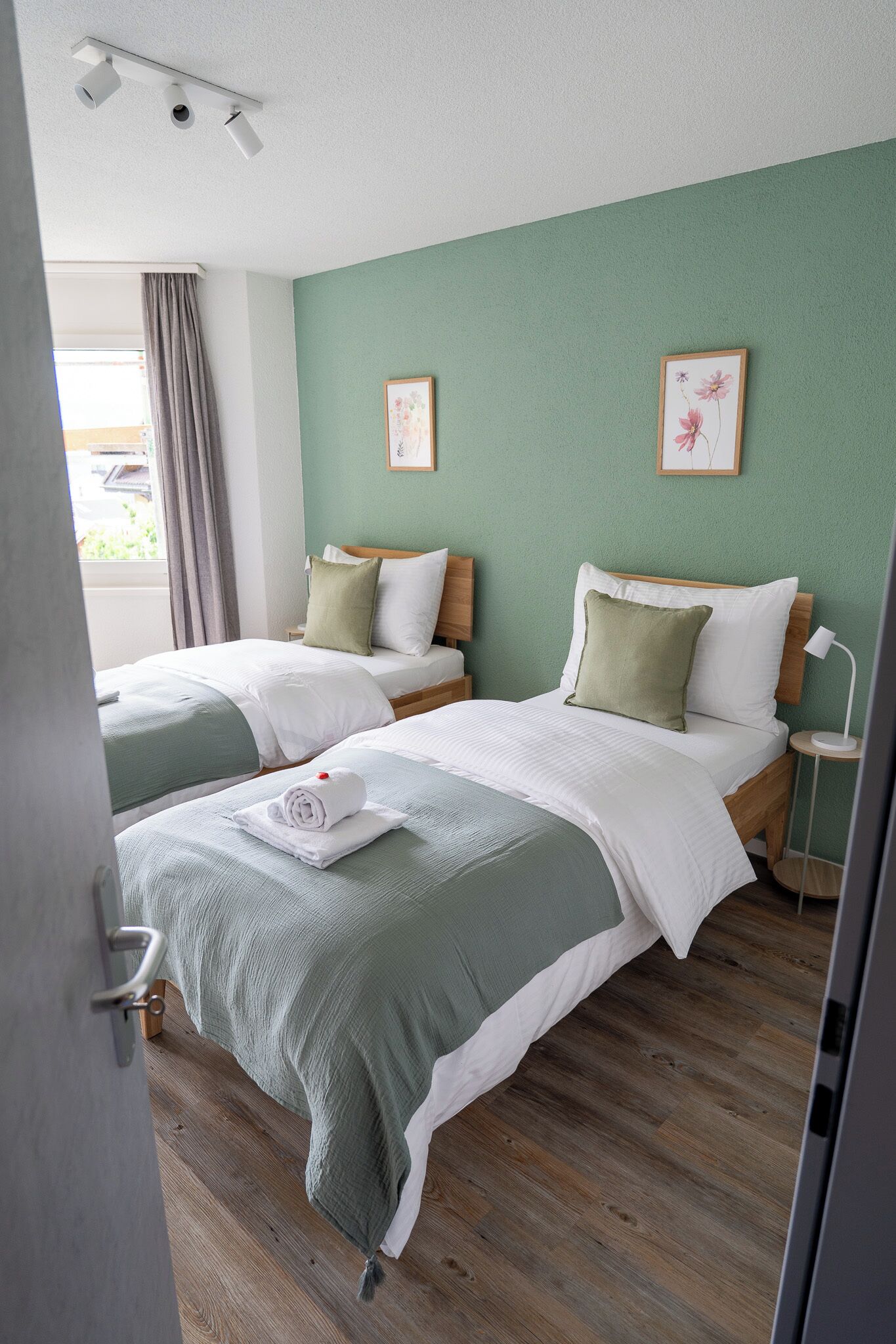 Ein Hotelzimmer mit zwei Betten, einer grünen Wand und einem Fenster mit Vorhängen.