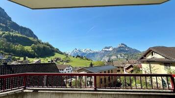 Un balcon avec une balustrade rouge donnant sur un paysage montagneux, avec des maisons et un ciel dégagé.