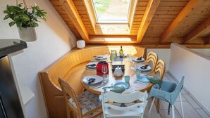 Un espace repas avec une table ronde, des chaises et une vue à travers une lucarne.