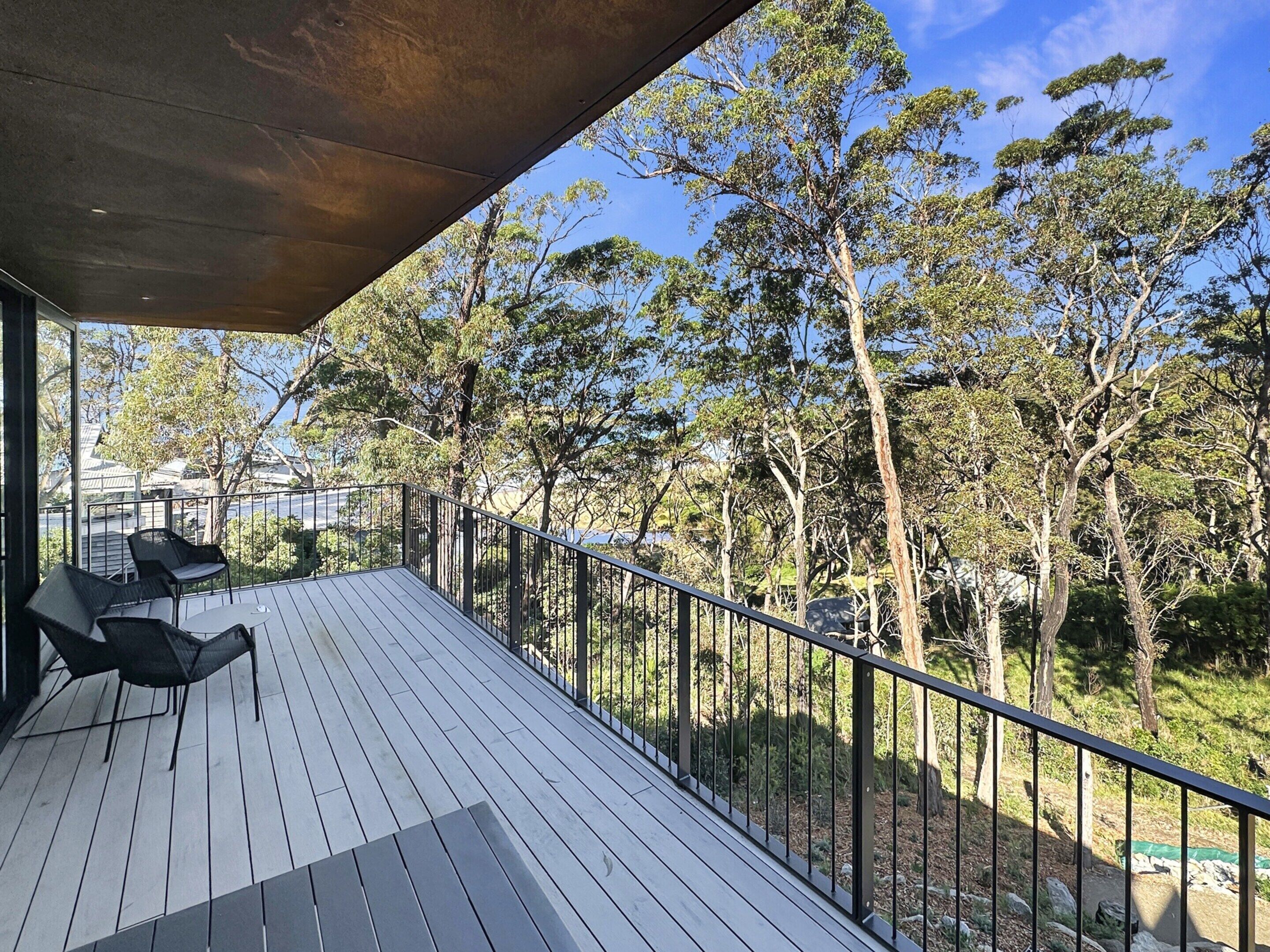 A wooden deck with outdoor furniture, a metal railing, and a view of trees and a distant building.