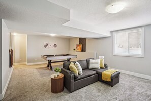 A living room with a pool table, a gray sofa, and a small side table.
