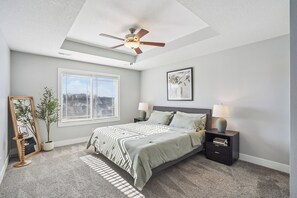 A bedroom with a bed, bedside tables, a ceiling fan, a window, and a potted plant.