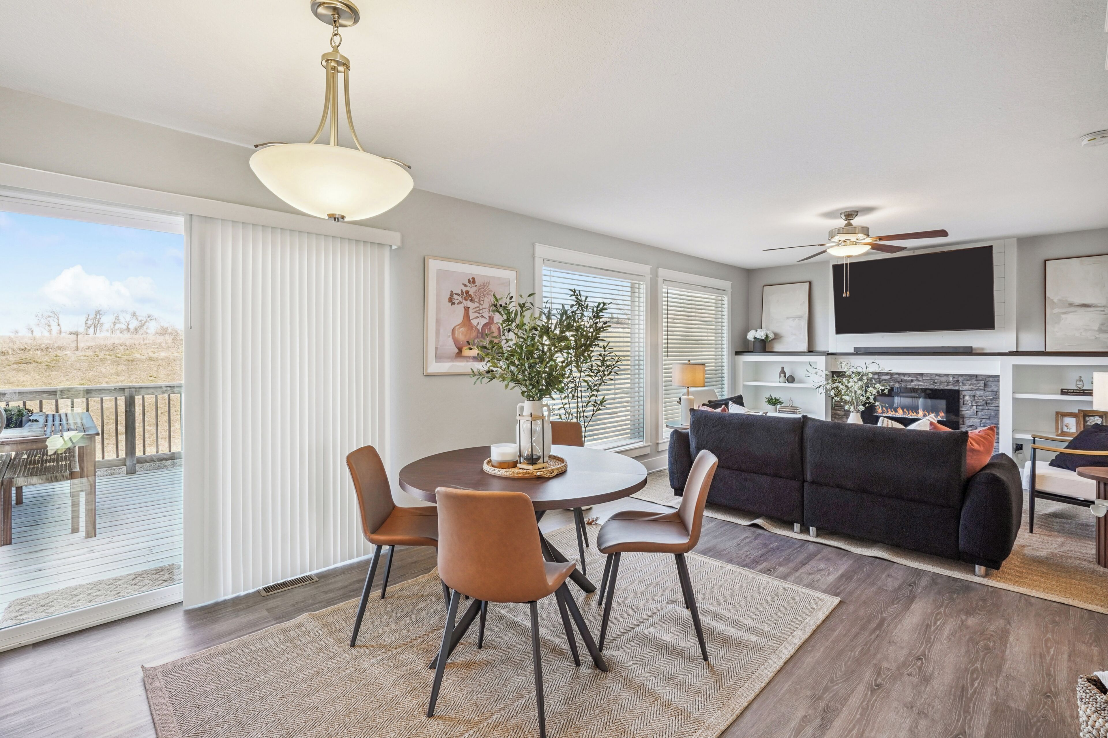 A modern living room with a fireplace, a dining area with a round table and chairs, and a balcony with outdoor furniture.
