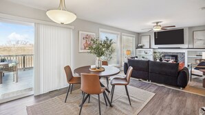 Ein modernes Wohnzimmer mit Kamin, einem Essbereich mit rundem Tisch und Stühlen sowie einem Balkon mit Gartenmöbeln.
