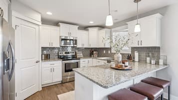 A modern kitchen with white cabinets, stainless steel appliances, a granite countertop, and a central island with stools.