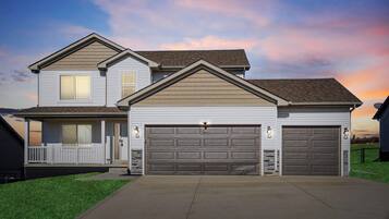 A two-story house with a garage, a covered porch, and a well-maintained lawn.
