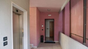 A corridor with a door, a trash bin, and a sign on the wall. - TUFFO in Laguna - Bilocale silenzioso con posto auto (Grado)