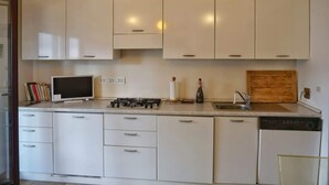 A modern kitchen with white cabinets, a gas stove, a dishwasher, and a pendant light. - TUFFO in Laguna - Bilocale silenzioso con posto auto (Grado)