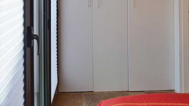 A room with a sliding door closet, a window with blinds, and a red bedspread. - TUFFO in Laguna - Bilocale silenzioso con posto auto (Grado)