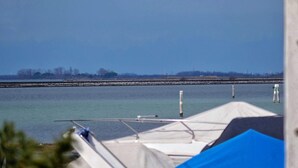 A marina with boats docked, a calm water body, and a distant shoreline with trees and structures. - TUFFO in Laguna - Bilocale silenzioso con posto auto (Grado)