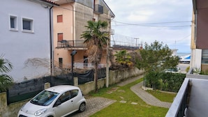 A residential area with a white car parked on a paved driveway, a palm tree, and a building with a balcony. - TUFFO in Laguna - Bilocale silenzioso con posto auto (Grado)