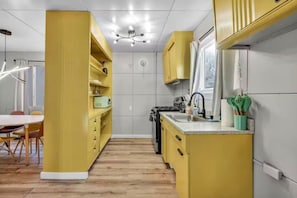 Eine moderne Küche mit gelben Schränken, ein Essbereich mit weißem Tisch und Stühlen sowie ein Holzboden.