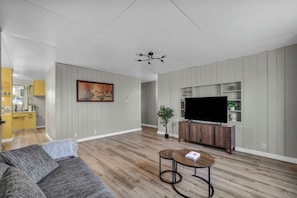 Ein Wohnzimmer mit einer Couch, einem Couchtisch, einem Fernseher auf einem Holzgestell und einem Gemälde an der Wand.
