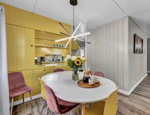 Ein moderner Essbereich mit einem weißen Tisch, gelben Stühlen, einer außergewöhnlichen Deckenleuchte und einer Vase mit Blumen.