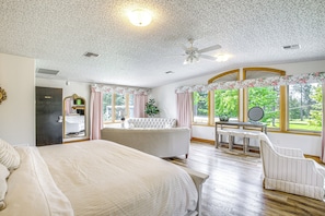 Un dormitorio con una cama grande, una zona de estar con una silla, un tocador y vistas a zonas verdes.