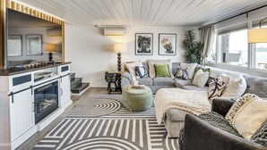 A modern living room with a fireplace, a sofa set, a coffee table, and a large window with a view. - Waterfront Cabin w/ Stunning Sound Views (University Place)