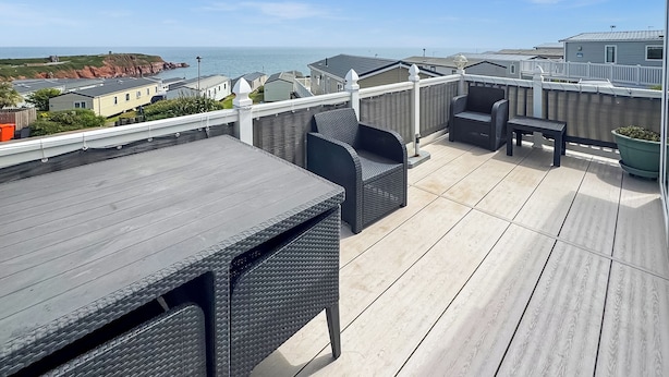 Ein Balkon mit Tisch und Stühlen, Blick auf das Meer und eine weiße Umzäunung.