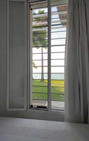 Ein Zimmer mit einem Bett, einem Fenster mit Blick auf einen Baum und einen Zaun, und einem teilweise zurückgezogenen Vorhang.