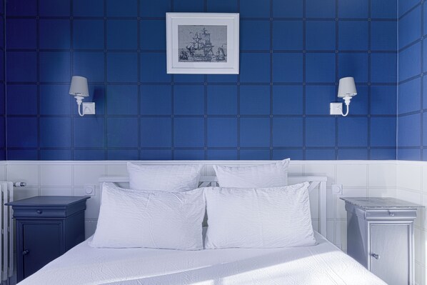 Een slaapkamer met een groot bed, witte beddengoed, twee nachtkastjes, een bijzettafeltje, een ingelijst schilderij aan de muur en twee wandlampen.