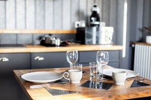 A dining table with plates, glasses, and cutlery, set against a kitchen backdrop with cabinets and appliances. - Coeur de Falaise 2 - 2-bedroom apartment downtown, private parking, EV charging station (Falaise)