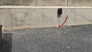 Un muro in cemento con un quadro elettrico nero e un cavo rosso.