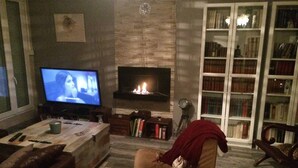Uma sala de estar com lareira, televisão, estante de livros e sofá.