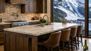 A kitchen with a large island, wooden cabinets, a stone backsplash, and a view of snow-capped mountains. - Ski-in Ski-out, hot tub, on the ski run, next to the chairlift. Epic views! #2 (Sandpoint)