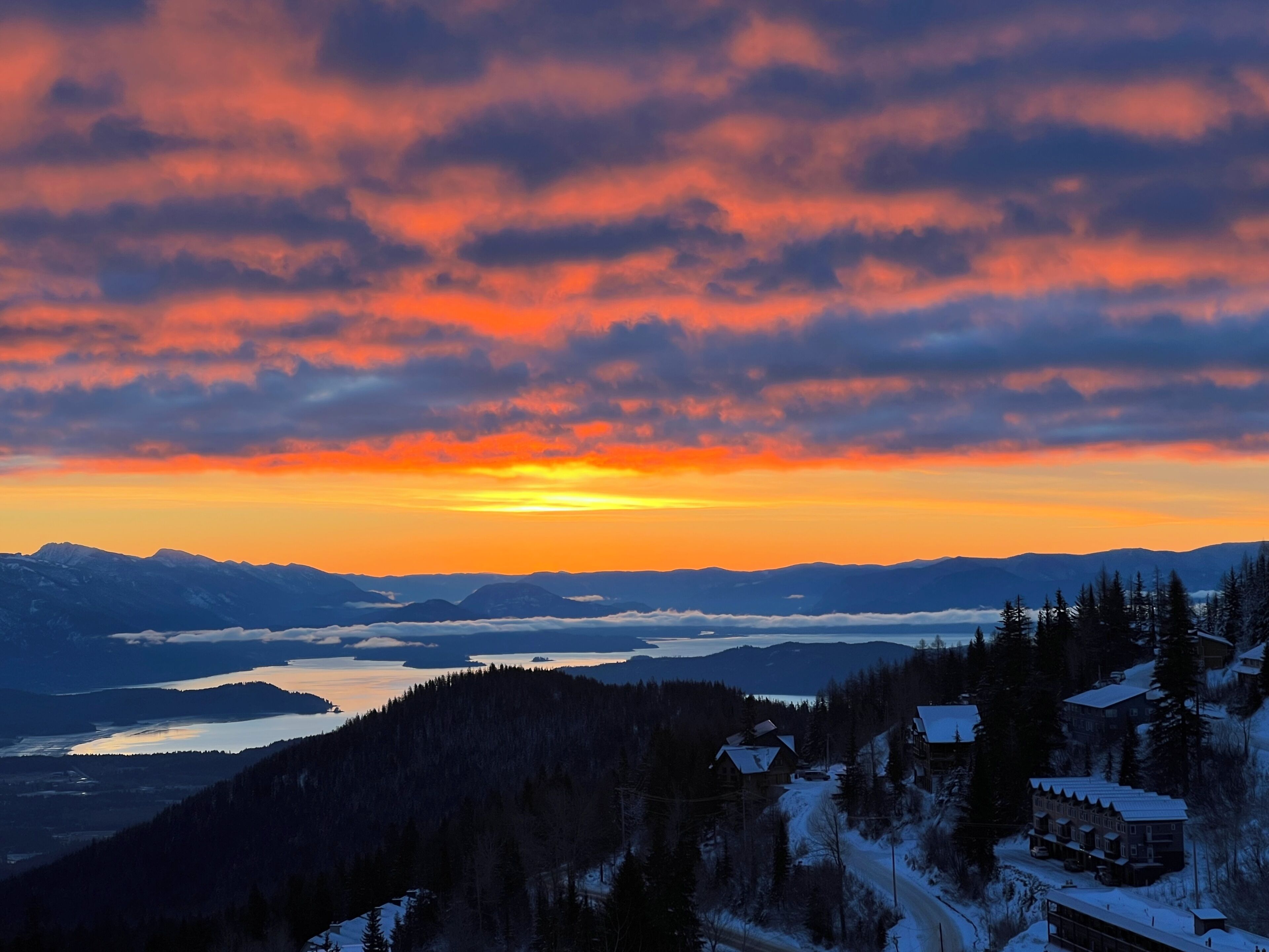 A mountain landscape with a sunset, snow-covered houses, and a lake.