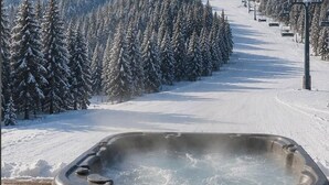 A hot tub on a wooden deck with a snowy mountain and ski slope in the background. - Ski-in Ski-out, hot tub, on the ski run, next to the chairlift. Epic views! #2 (Sandpoint)
