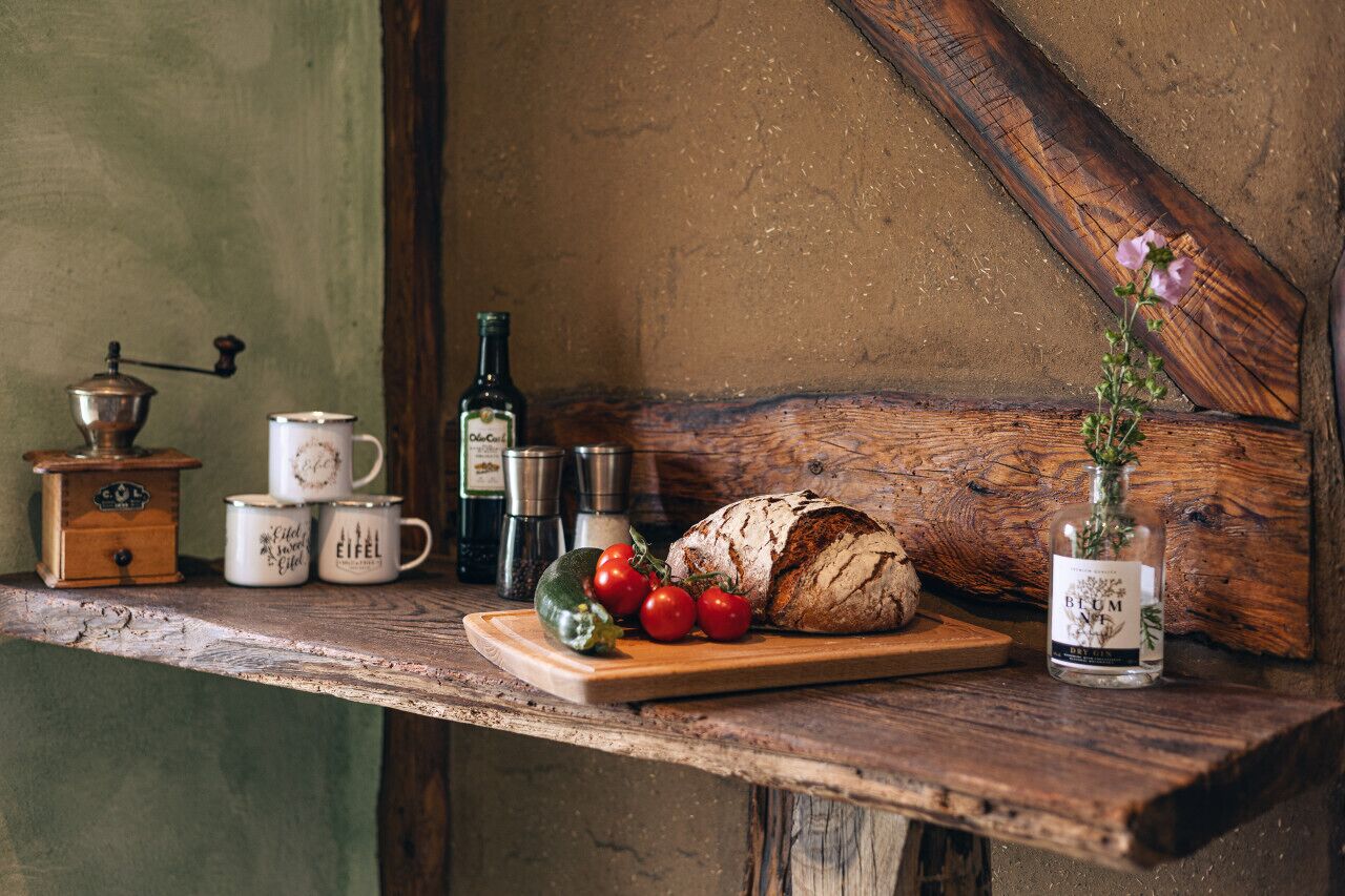 A rustic wooden table with a loaf of bread, tomatoes, a bottle of olive oil, and a vase with flowers.