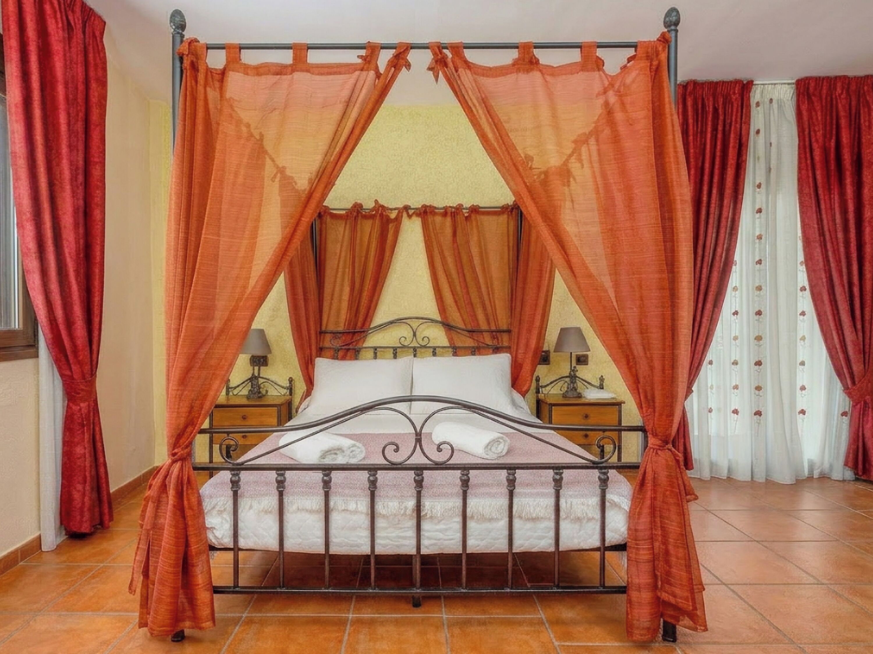 A bed with a metal frame and a canopy, two bedside tables with lamps, and curtains on the windows.