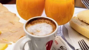 A breakfast setting with a cup of coffee, two glasses of orange juice, a sandwich, and a spoon on a table.