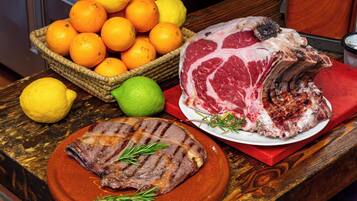 Taula amb un plat de carn rostida al centre, un plat de carn a la brasa i una cistella d'albercocs i limones.