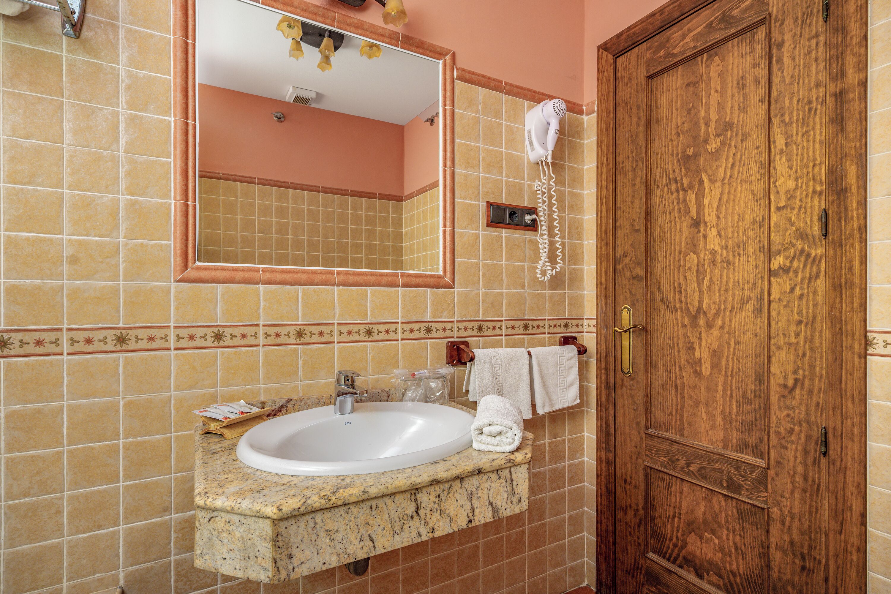 Un bany amb un lavabo de marbre, un mirall, un assecador d'eixugat i una porta de fusta.