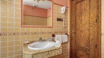 Un bany amb un lavabo de marbre, un mirall, un assecador d'eixugat i una porta de fusta.