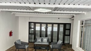 Eine überdachte Terrasse mit Steinboden, einer Couch, zwei Stühlen und einem Feuerlöscher.