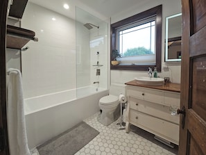 A modern bathroom with a glass-enclosed shower, a toilet, a sink with a wooden countertop, and a large mirror above the sink.