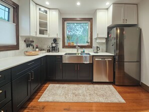 A compact kitchen with dark cabinets, a stainless steel refrigerator, and a window with a view of trees.
