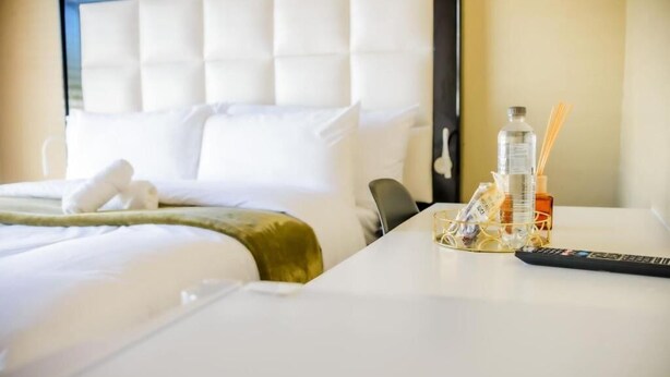 Quarto de hotel com cama, mesa de cabeceira com controle remoto, garrafa e recipiente de vidro.