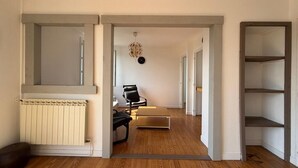 A hallway with a radiator, a wooden floor, a chair, a coffee table, and a hanging light fixture. - Les Toits de Bayonne - Mountain view (BAYONNE)