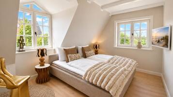 A bedroom with a large bed, two windows, a chair, a lamp, and a painting on the wall.