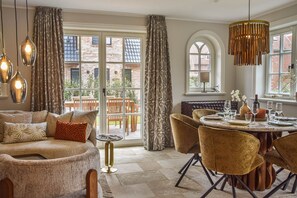 Ein gemütliches Wohnzimmer mit einer Couch, einem Esstisch, Stühlen und Blick auf einen Backsteininnenhof durch große Fenster.