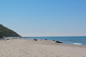 En strand med klart himmel, sandet bredde og klippeudspring.