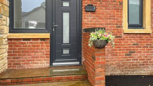 A brick building with a black door, a window, and a wall-mounted light fixture. - Barncroft Retreat - UK51693 (High Seaton, near Workington)