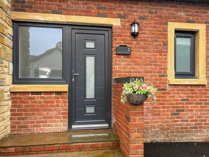A brick building with a black door, a window, and a wall-mounted light fixture. - Barncroft Retreat - UK51693 (High Seaton, near Workington)
