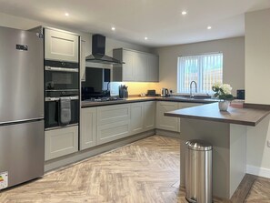 A modern kitchen with stainless steel appliances, a built-in oven, and a large window. - Barncroft Retreat - UK51693 (High Seaton, near Workington)