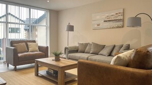 A living room with a sofa, armchair, and coffee table, a painting on the wall, and a lamp. - Barncroft Retreat - UK51693 (High Seaton, near Workington)