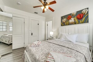 Ein Schlafzimmer mit einem Bett, einem Deckenventilator, einem Gemälde von Tulpen und einer weißen Tür.