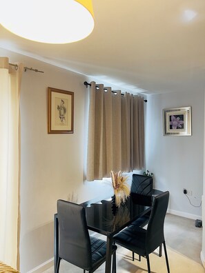 A dining area with a black table, black chairs, a vase with dried plants, a framed picture on the wall, and a window with beige curtains. - Deluxe Private Room in a flat W Fast WiFi, Netflix, Free Parking (West Midlands)